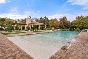 A pool area with a covered patio, a stone building, and surrounding trees. - Landing | Stunning 2BD, Pool, Game Room (Cedar Park)