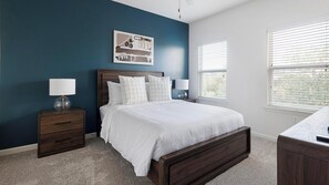 A bedroom with a dark blue wall, a wooden bed frame, white bedding, two bedside tables with lamps, and a window with blinds. - Landing | Stunning 2BD, Pool, Game Room (Cedar Park)