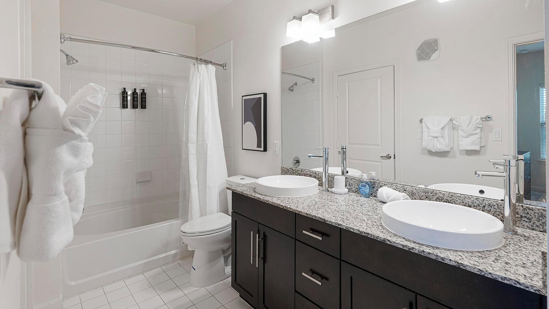 A modern bathroom with a walk-in shower, two sinks, a large mirror, and dark cabinetry.