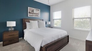 A bedroom with a large bed, two bedside tables with lamps, a wall art piece, and a window with blinds. - Landing | Modern 2BD, Gym, Clubhouse (Cedar Park)