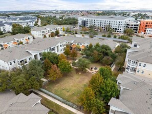 A residential area with multiple apartment buildings, a central grassy courtyard, and surrounding trees. - Landing | Stunning 2BD, Pool, Game Room (Cedar Park)