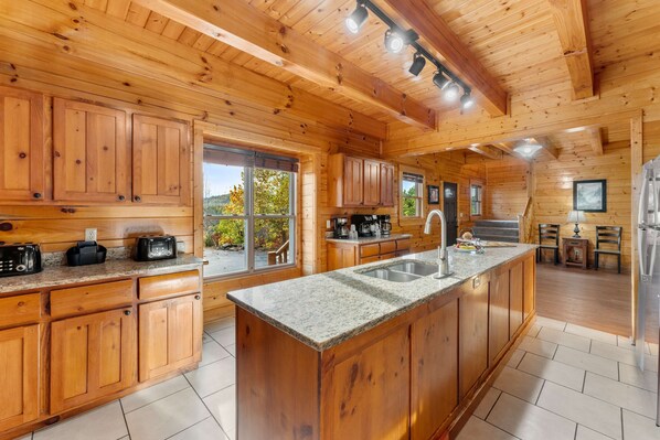 Ein Interieur einer Holzhütte mit einer Küche, die sich durch Granitarbeitsplatten, Holzschränke und eine zentrale Kochinsel mit Spüle auszeichnet.