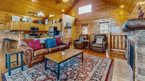 A cozy cabin interior with a wooden ceiling, a fireplace, a dining area, and a kitchen with wooden cabinets and a microwave. - Lovely Cabin, Sleep 6・Hot Tub・Mtn View・Pool Access (Sevierville)