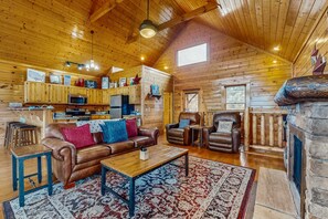 A cozy cabin interior with a wooden ceiling, a fireplace, a dining area, and a kitchen with wooden cabinets and a microwave. - Lovely Cabin, Sleep 6・Hot Tub・Mtn View・Pool Access (Sevierville)