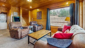 A cozy cabin interior with wooden walls and ceiling, a sofa, two armchairs, a small table, and a window with curtains. - Lovely Cabin, Sleep 6・Hot Tub・Mtn View・Pool Access (Sevierville)