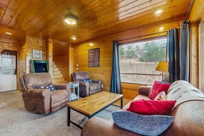 A cozy cabin interior with wooden walls and ceiling, a sofa, two armchairs, a small table, and a window with curtains. - Lovely Cabin, Sleep 6・Hot Tub・Mtn View・Pool Access (Sevierville)