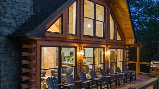 A log cabin with a deck featuring Adirondack chairs, a stone wall, and a large window overlooking the interior. - Mountain Cabin Retreat・Hot Tub・Arcade・Fireplace (Sevierville)
