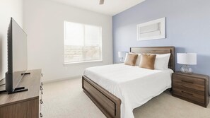 Quarto com cama, mesas de cabeceira, luminária, televisão e janela com persianas.