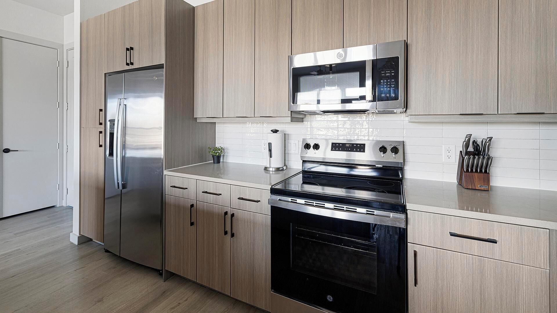 A modern kitchen with stainless steel appliances, wooden cabinetry, and a white tiled backsplash.