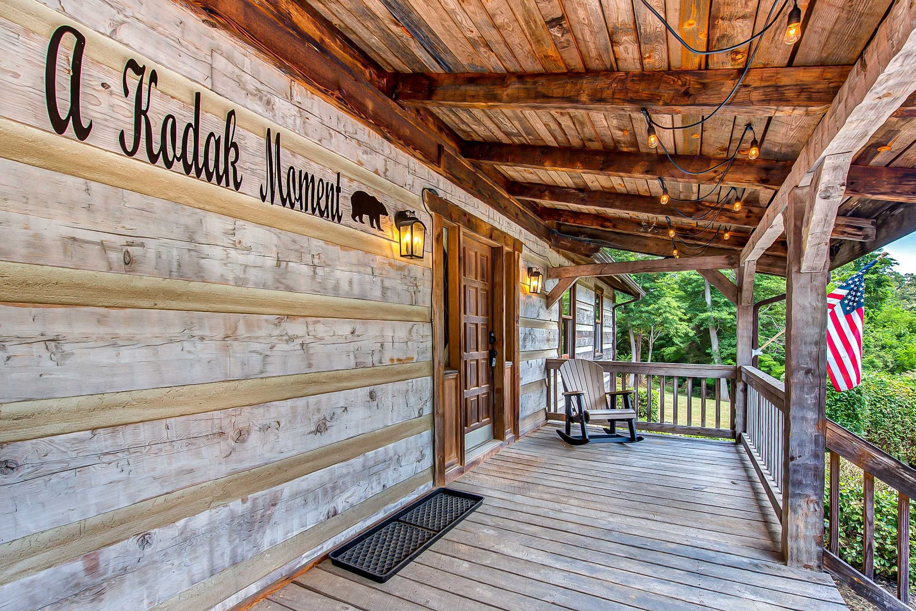 A wooden cabin with a sign reading "A Kodak Moment" and a porch with a bench and an American flag.