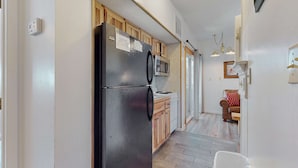 Eine kleine Küche mit einem schwarzen Kühlschrank, Holzschränken und einer Mikrowelle.