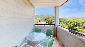 Ein Balkon mit rundem Tisch und vier Stühlen, mit Blick auf eine grüne Landschaft mit Bäumen und Gebäuden.