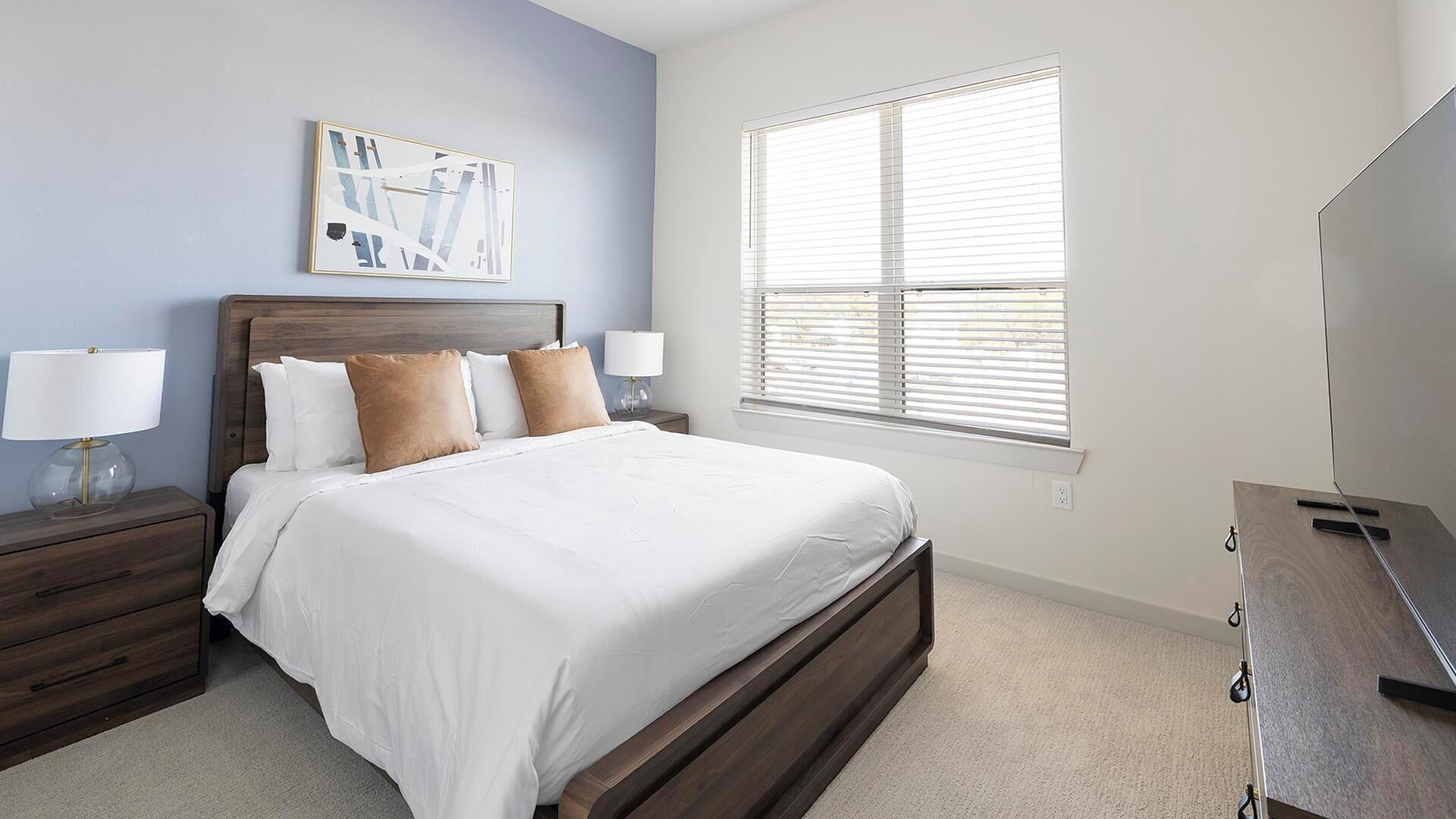 A bedroom with a bed, nightstands, a dresser, a painting, and a window with blinds.