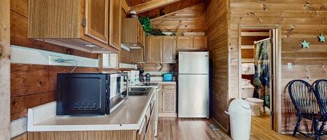 A compact kitchen with wooden cabinets, a microwave, a refrigerator, and a sink.