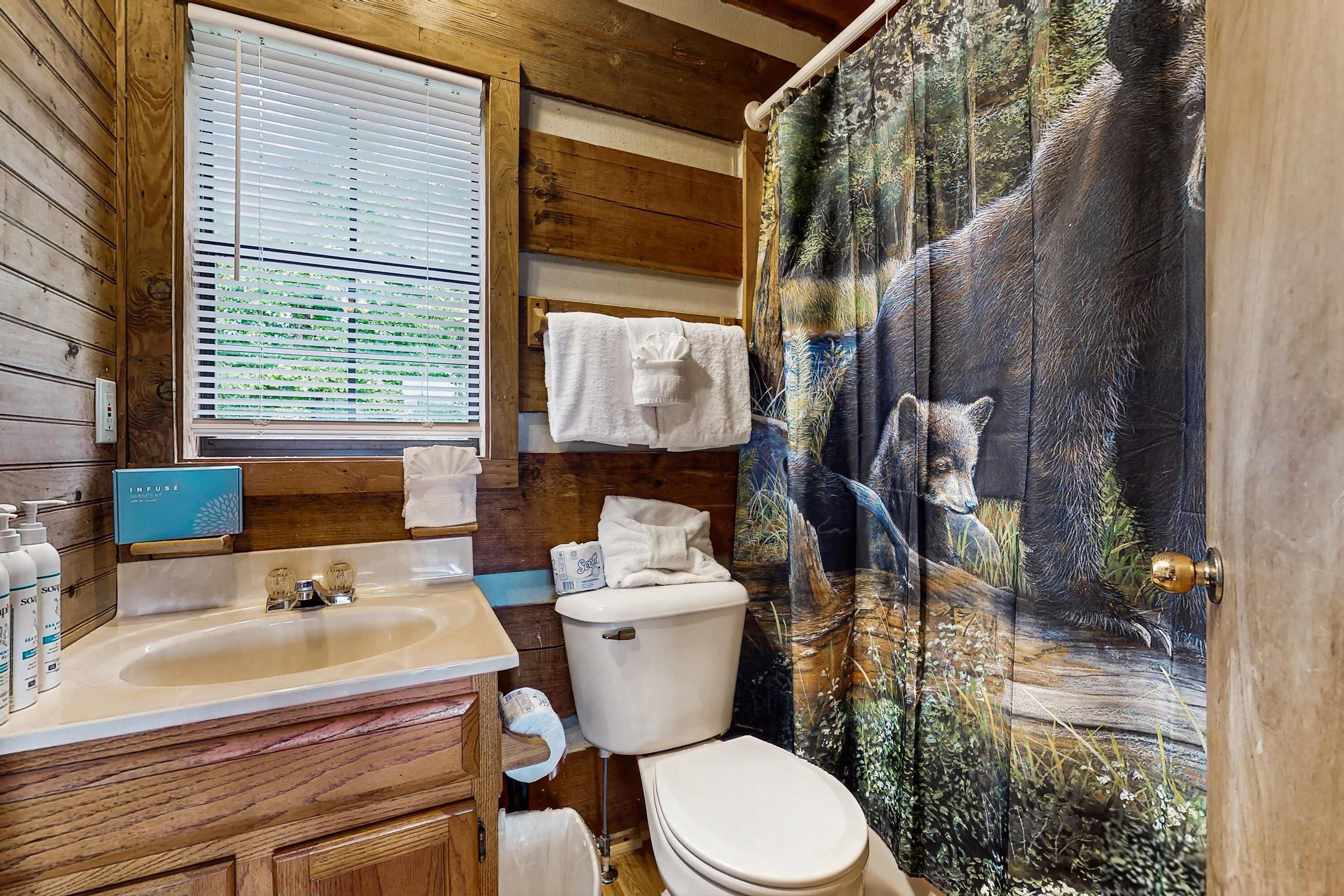 Een badkamer met houten wanden, een wastafel met toiletartikelen, een toilet en een douchegordijn met een ontwerp van een beer.
