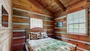 A log cabin bedroom with a wooden bed, two windows, and a quilt with animal prints. - Secluded Smoky Mtn Cabin Escape・Views・Pet Friendly (Townsend)