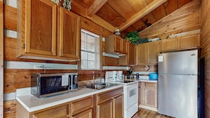 A wooden cabin-style kitchen with a microwave, stove, sink, and refrigerator. - Secluded Smoky Mtn Cabin Escape・Views・Pet Friendly (Townsend)