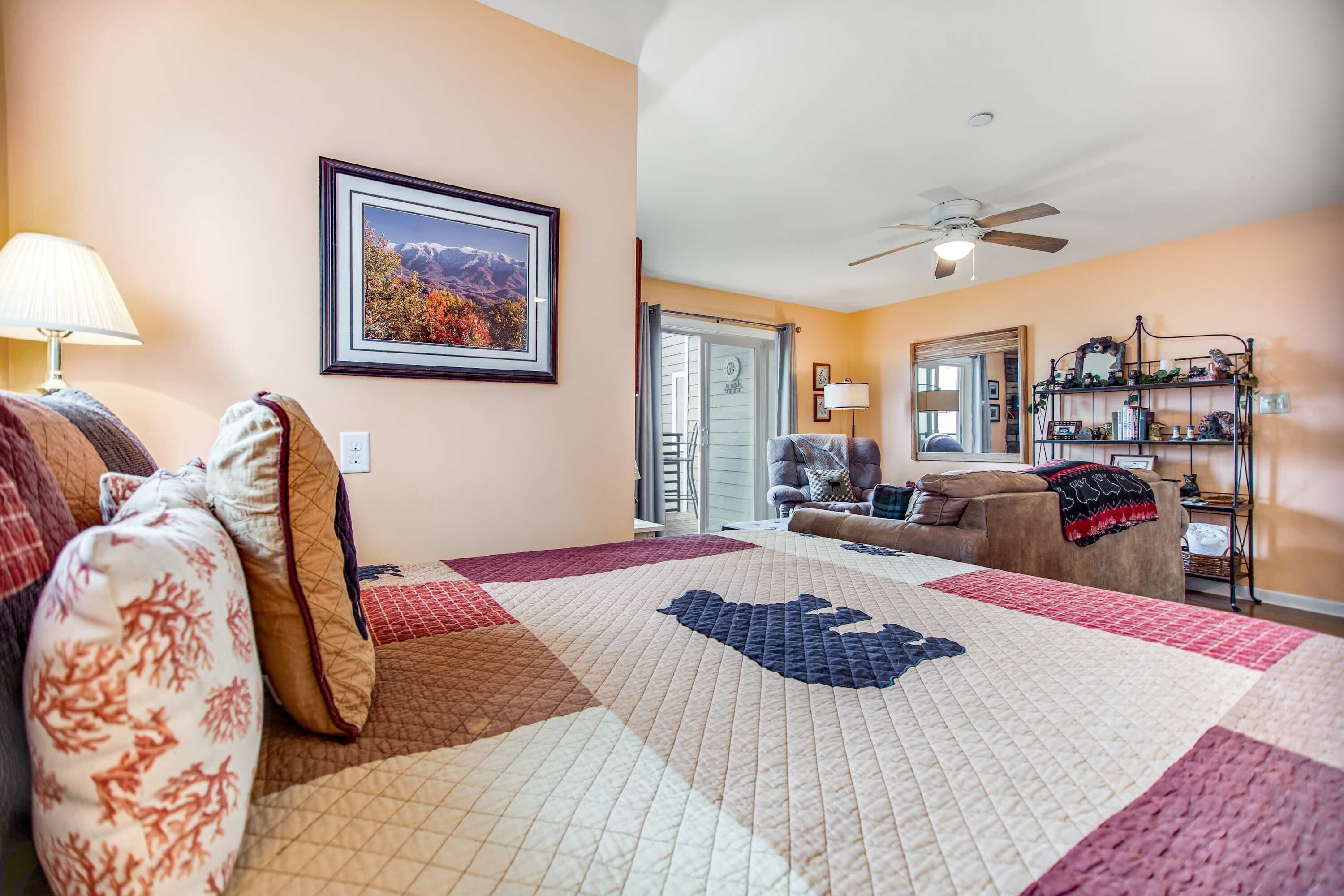 Une chambre d’hôtel avec un grand lit, un canapé, un fauteuil, un ventilateur de plafond, un tableau encadré au mur et une petite table avec une lampe.