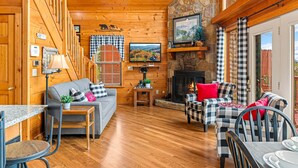 A cozy log cabin interior with a fireplace, wooden walls, a sofa, and a dining area. - Bearfoot Inn, Sleeps 6・Stunning Views・Games (Sevierville)