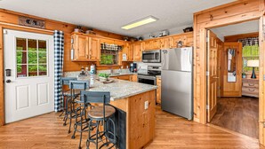 A kitchen with wooden cabinets, a granite countertop, a stainless steel refrigerator, and a bar area with stools. - Bearfoot Inn, Sleeps 6・Stunning Views・Games (Sevierville)
