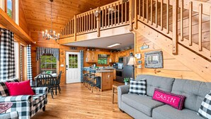 A cabin interior with a dining area, kitchen, and a gray sofa with a 'CABIN' pillow. - Bearfoot Inn, Sleeps 6・Stunning Views・Games (Sevierville)