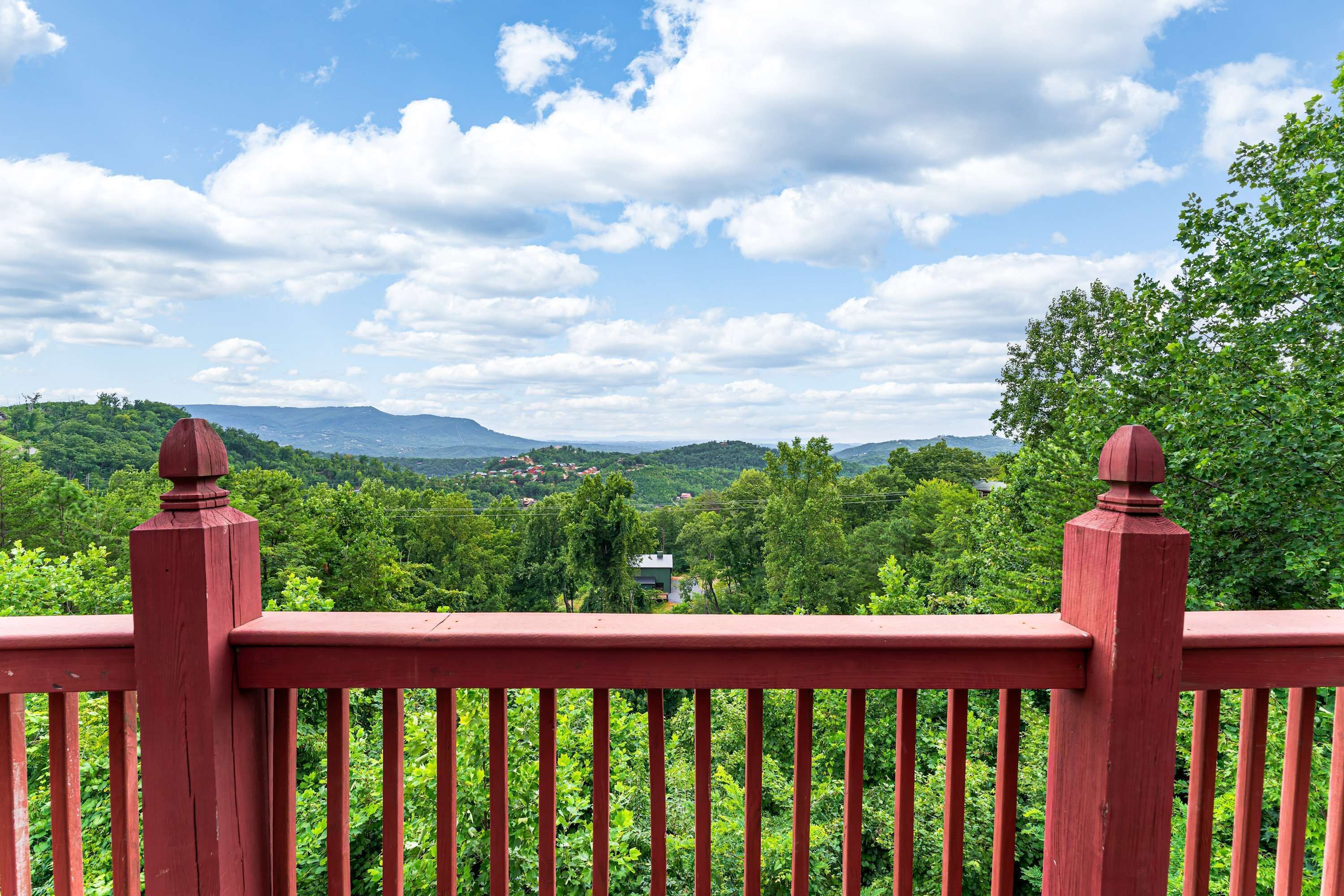 A red wooden railing overlooking a lush green landscape with hills and a clear sky.