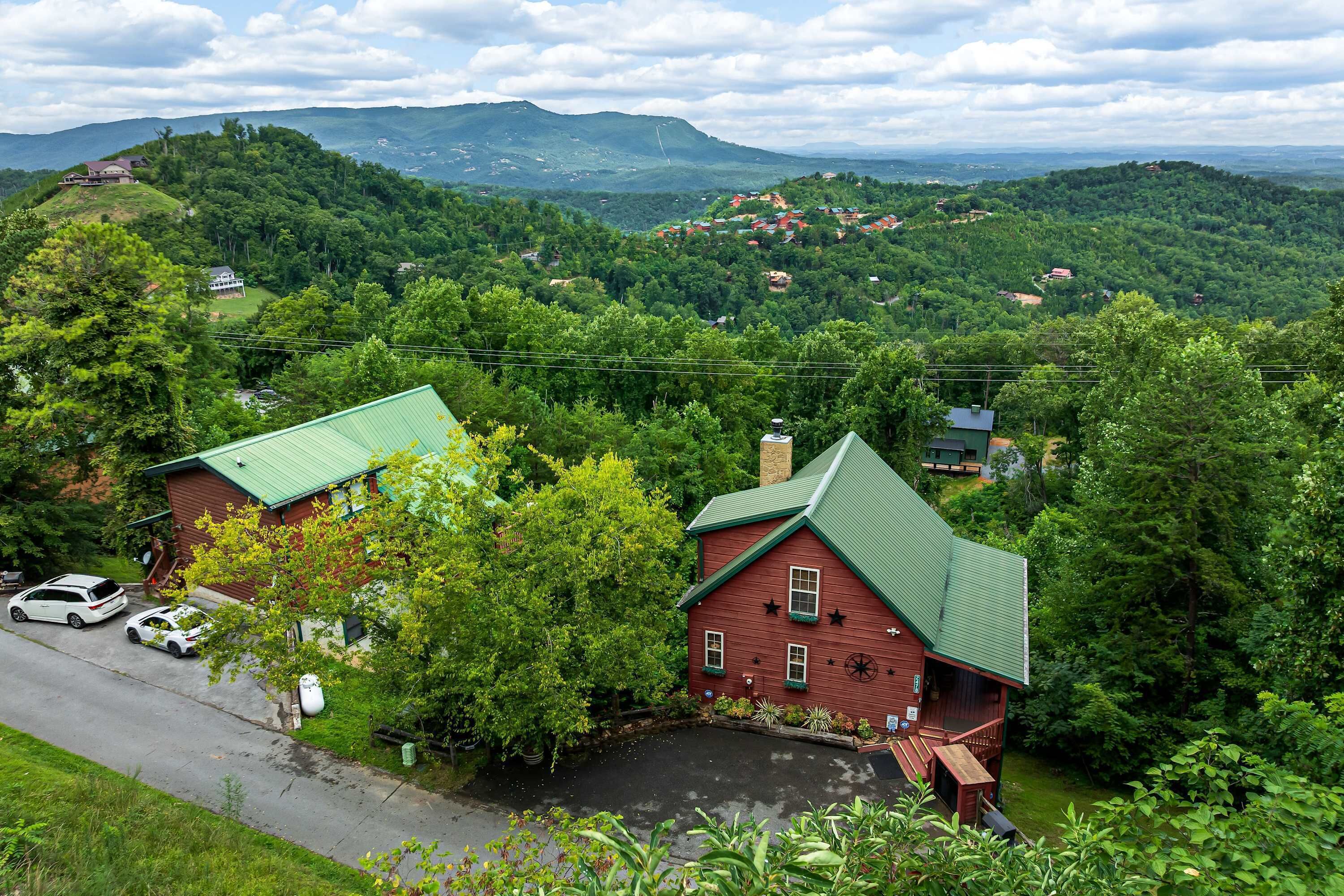 A red house with a green roof, surrounded by lush greenery and a view of distant hills.
