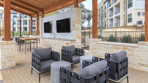 An outdoor patio with stone walls, a built-in grill, and outdoor seating. - Landing | Stunning 1BD, Gym (San Antonio)