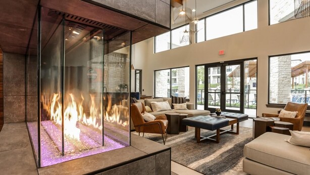 A modern lounge area with a glass fireplace, comfortable seating, and large windows offering views of the outside. - Landing | Stunning 1BD, Gym (San Antonio)