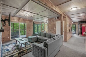 A log cabin interior with a sectional sofa, a small table, and a chandelier. - Cozy Mtn View Home, Sleeps 15, Hot Tub, Games, Gym (Sevierville)