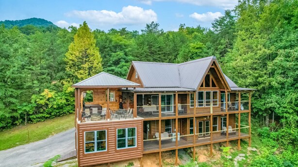 Une cabane en rondins à plusieurs étages, dotée d’un balcon, entourée d’une forêt dense et avec une montagne en arrière-plan.