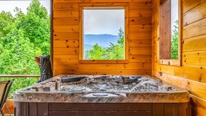 Une cabane en bois dotée d’un bain à remous et d’une fenêtre donnant sur une zone boisée.