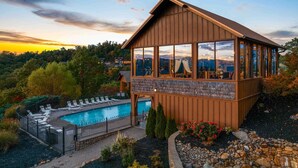 A wooden cabin with a pool, surrounded by trees and a view of the mountains. - Sleeps 116 | Smoky Mountain Views | 4 Hot Tubs | 2 Game Rooms | (Sevierville)