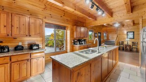 A wooden cabin interior with a kitchen featuring granite countertops, wooden cabinets, and a large island. - Sleeps 116 | Smoky Mountain Views | 4 Hot Tubs | 2 Game Rooms | (Sevierville)