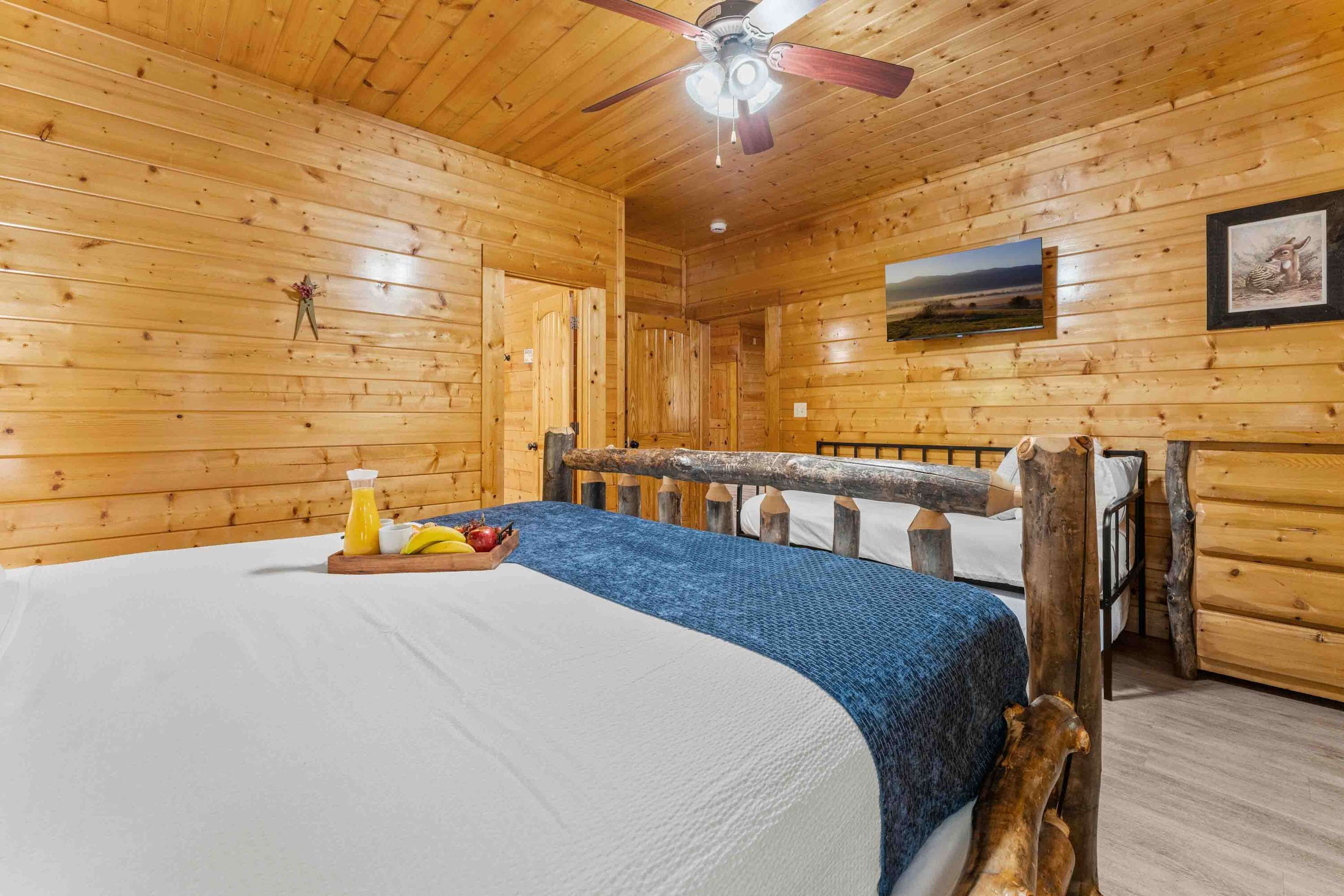 A wooden cabin room with a bed, a ceiling fan, and a framed picture on the wall.
