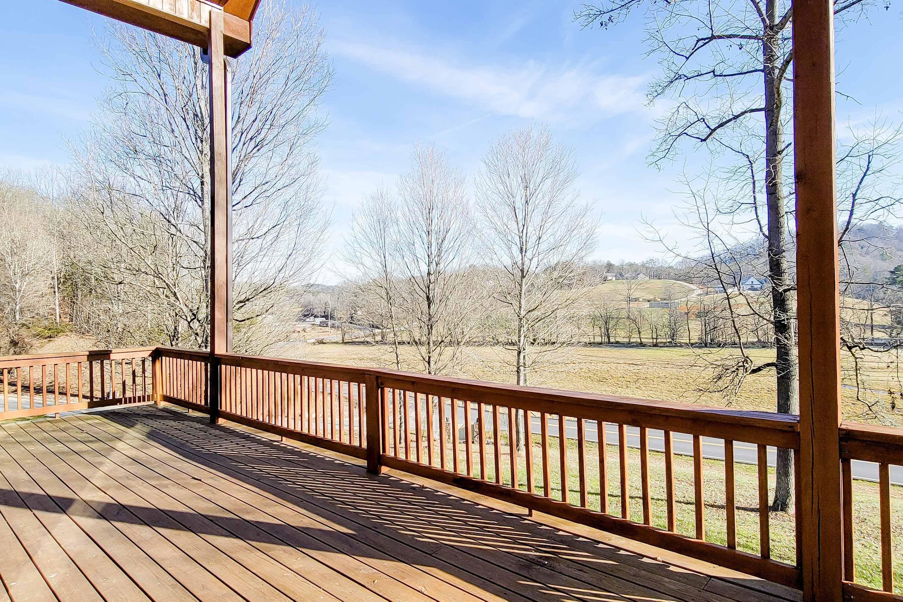 A wooden deck with a railing overlooking a rural landscape with trees and a distant house.