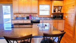 Una cucina con mobili in legno, un forno a microonde, un lavello e un'isola in vetro con due sedie.