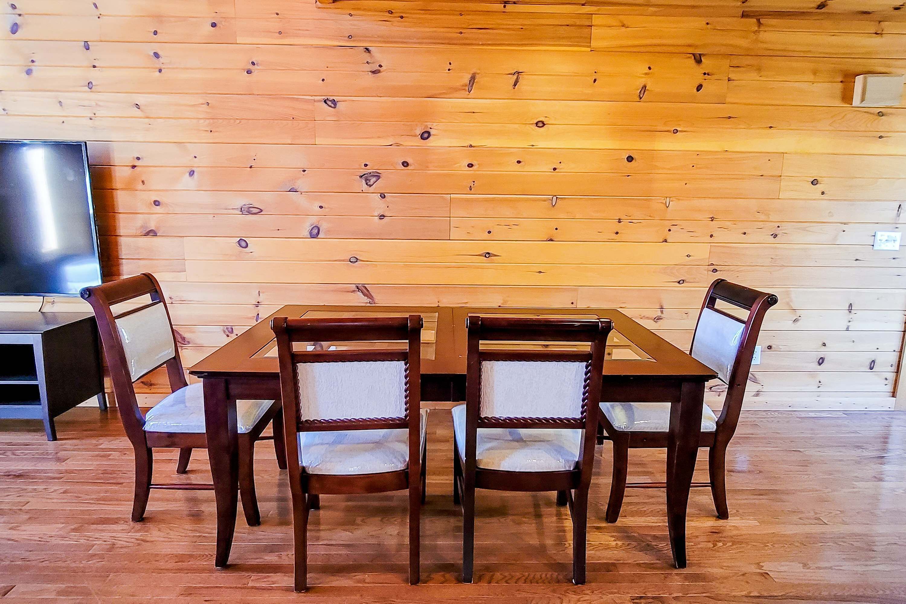A wooden-paneled wall, a wooden dining table with four chairs, and a television on the left.