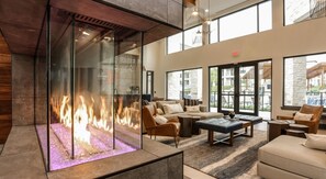 Uma área de estar moderna com lareira de vidro, assentos confortáveis e grandes janelas com vista para o exterior.