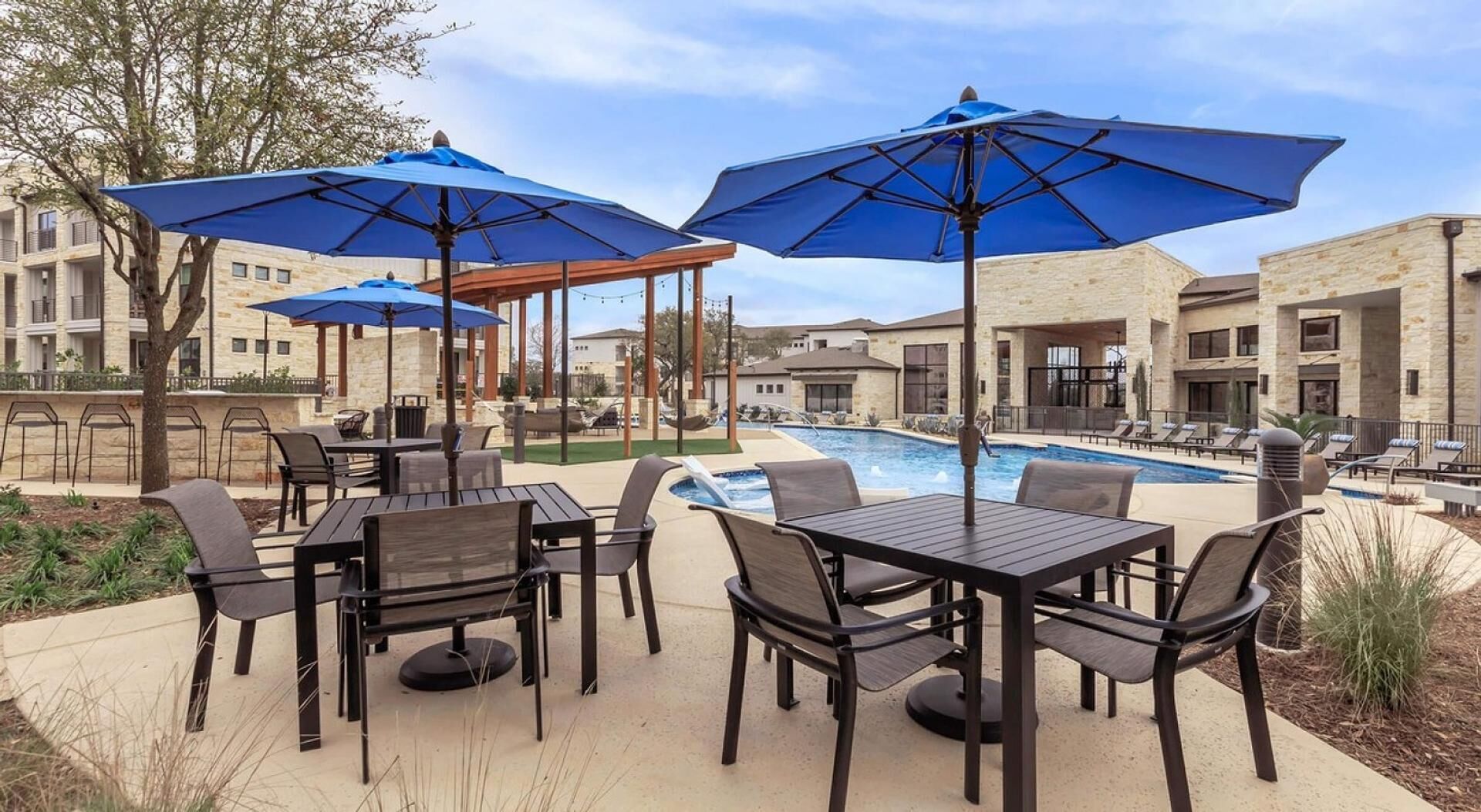 Un espace extérieur avec une piscine, des tables et des chaises, des parasols bleus et un kiosque.