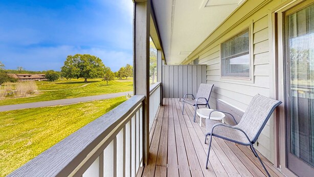 A wooden deck with two chairs and a small table, overlooking a grassy area with trees and a building in the distance. - Inviting & Cozy Studio, Sleep 4, Shared Gym & Games (Baneberry)