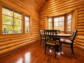 A log cabin interior with a dining table and chairs, large windows, and a wooden floor. - Mountain Views, Hot Tub & Dog-Friendly Cabin (Gatlinburg)