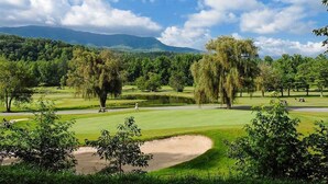 Un campo da golf con uno stagno, alberi e montagne sullo sfondo.
