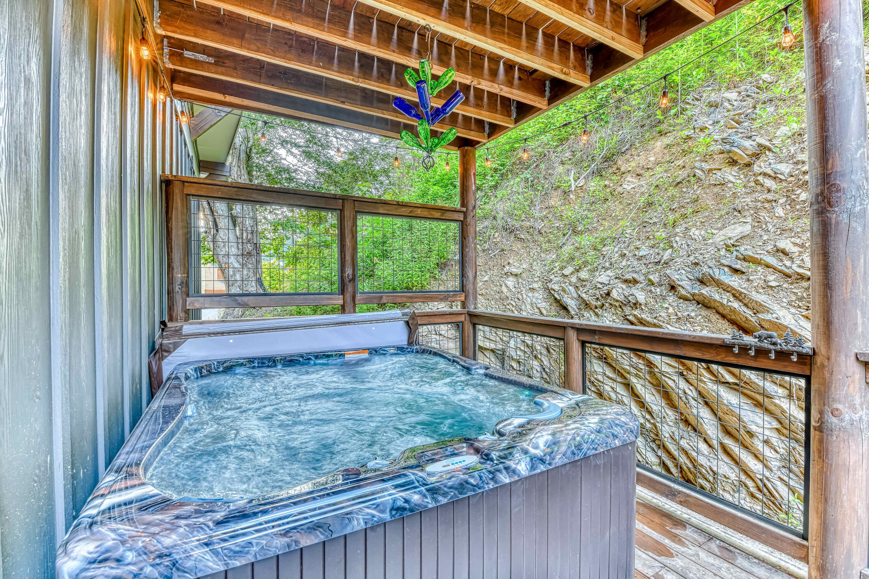 A hot tub with a wooden deck and a view of a rocky hillside.