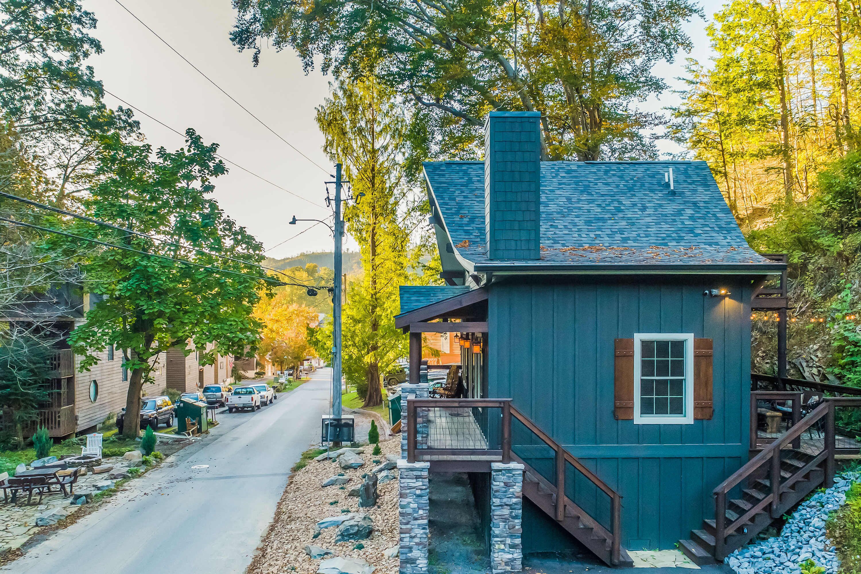 A small, two-story building with a dark blue exterior and a chimney, located on a street with parked cars and trees.