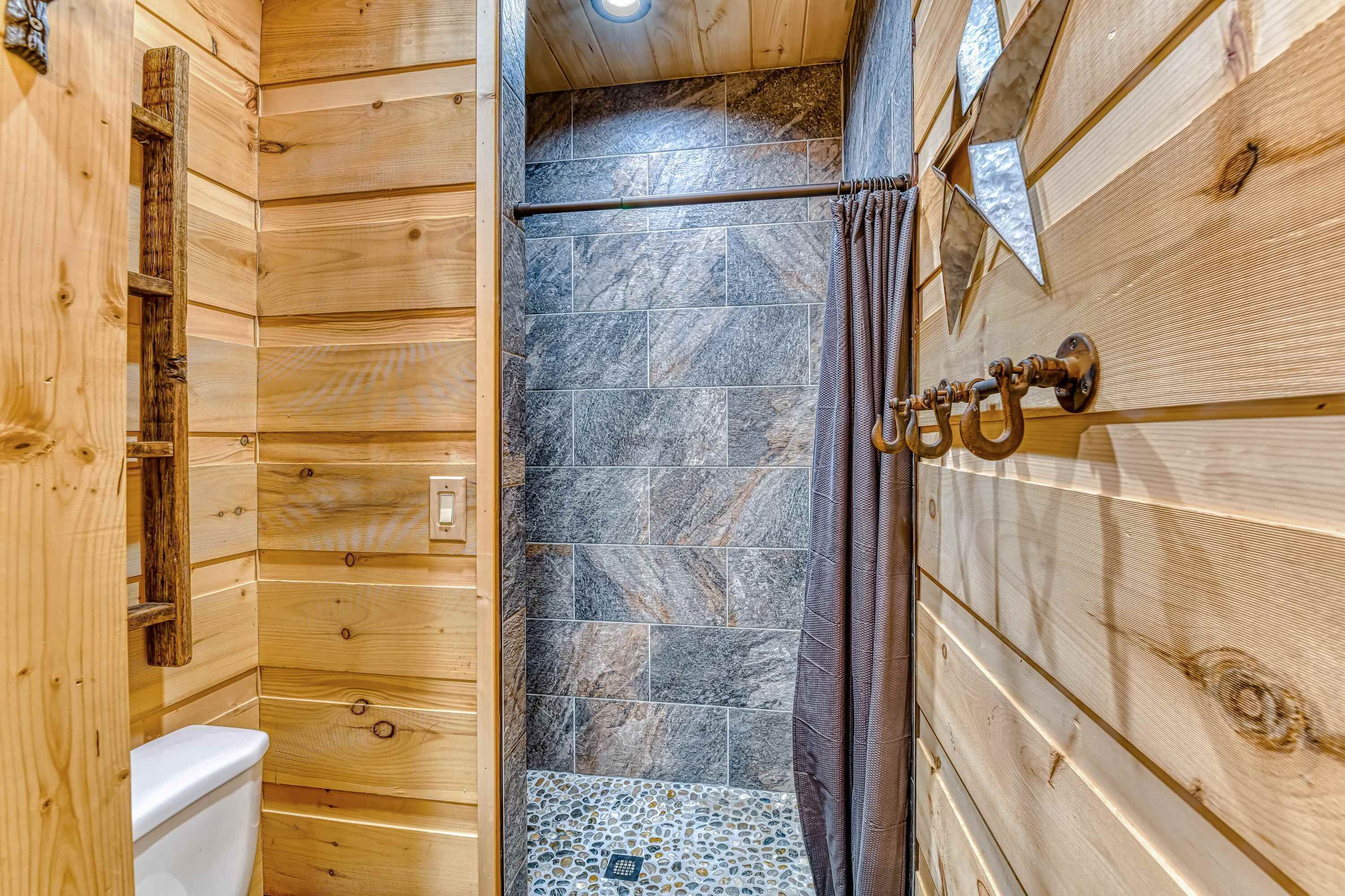 A wooden cabin bathroom with a shower area, a toilet, and a wooden door with a towel rack.