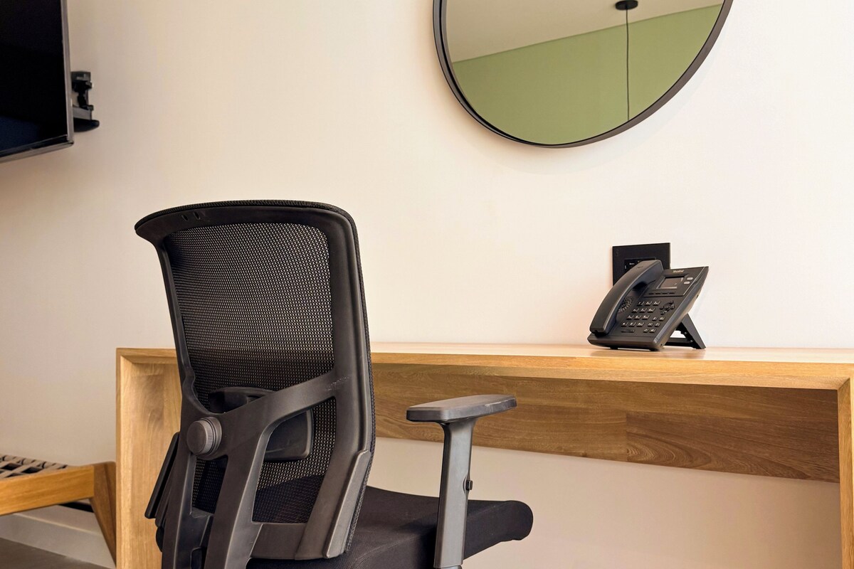 A modern office chair with wheels, a wooden desk, a telephone, and a wall-mounted mirror.