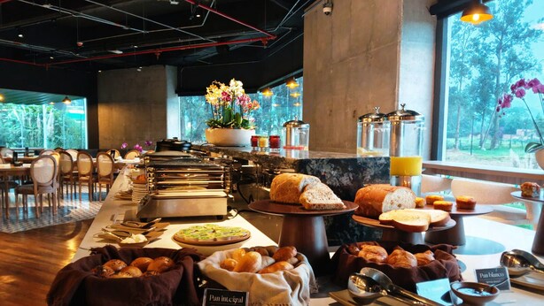 A breakfast buffet with various bread and pastries, a whole wheat bread sign, and a view of the outdoors through large windows. - Hotel B3 Sibelius (Chía)