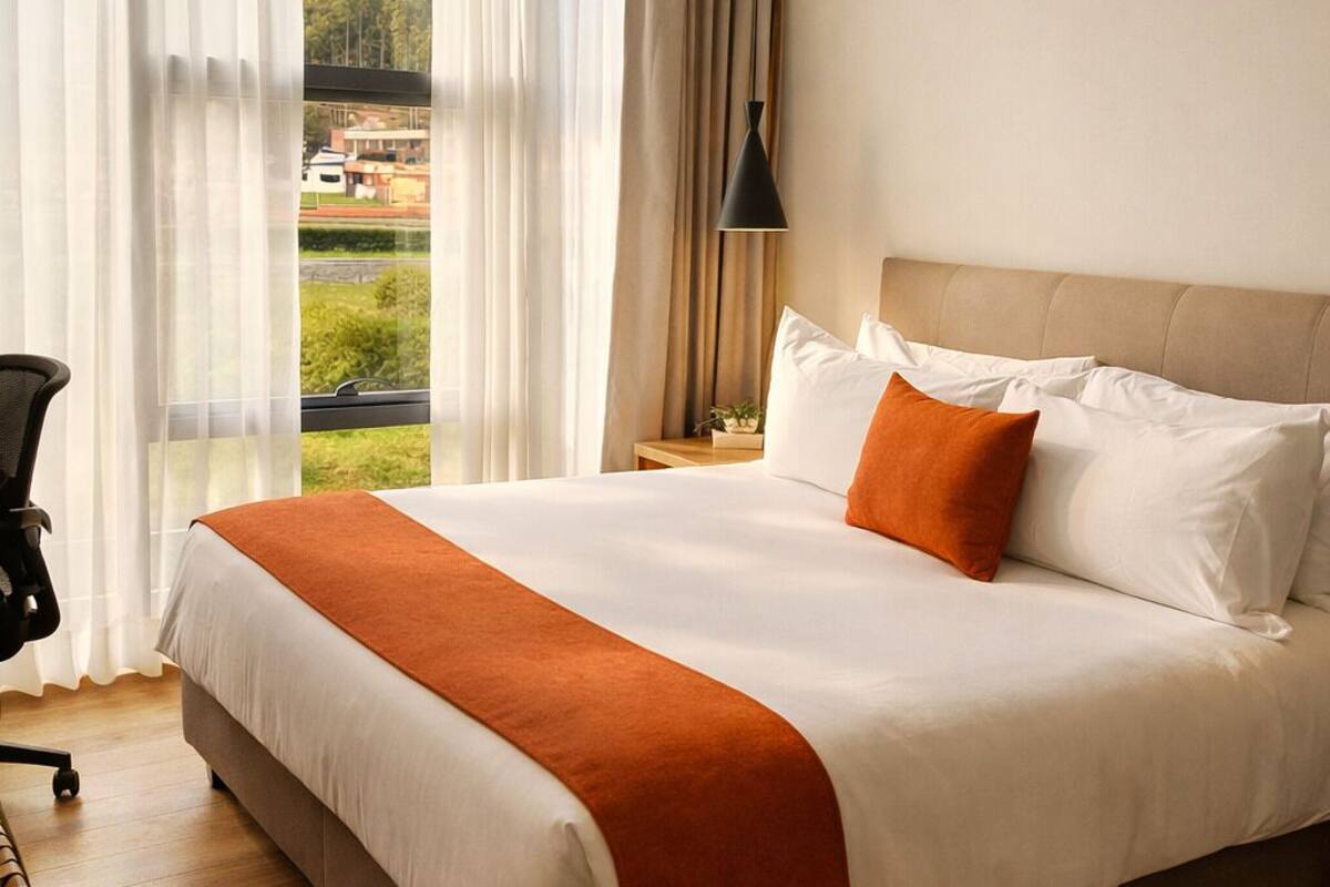 Ein Hotelzimmer mit einem großen Bett, einem Schreibtisch, einem Sessel und Blick auf eine Landschaft.