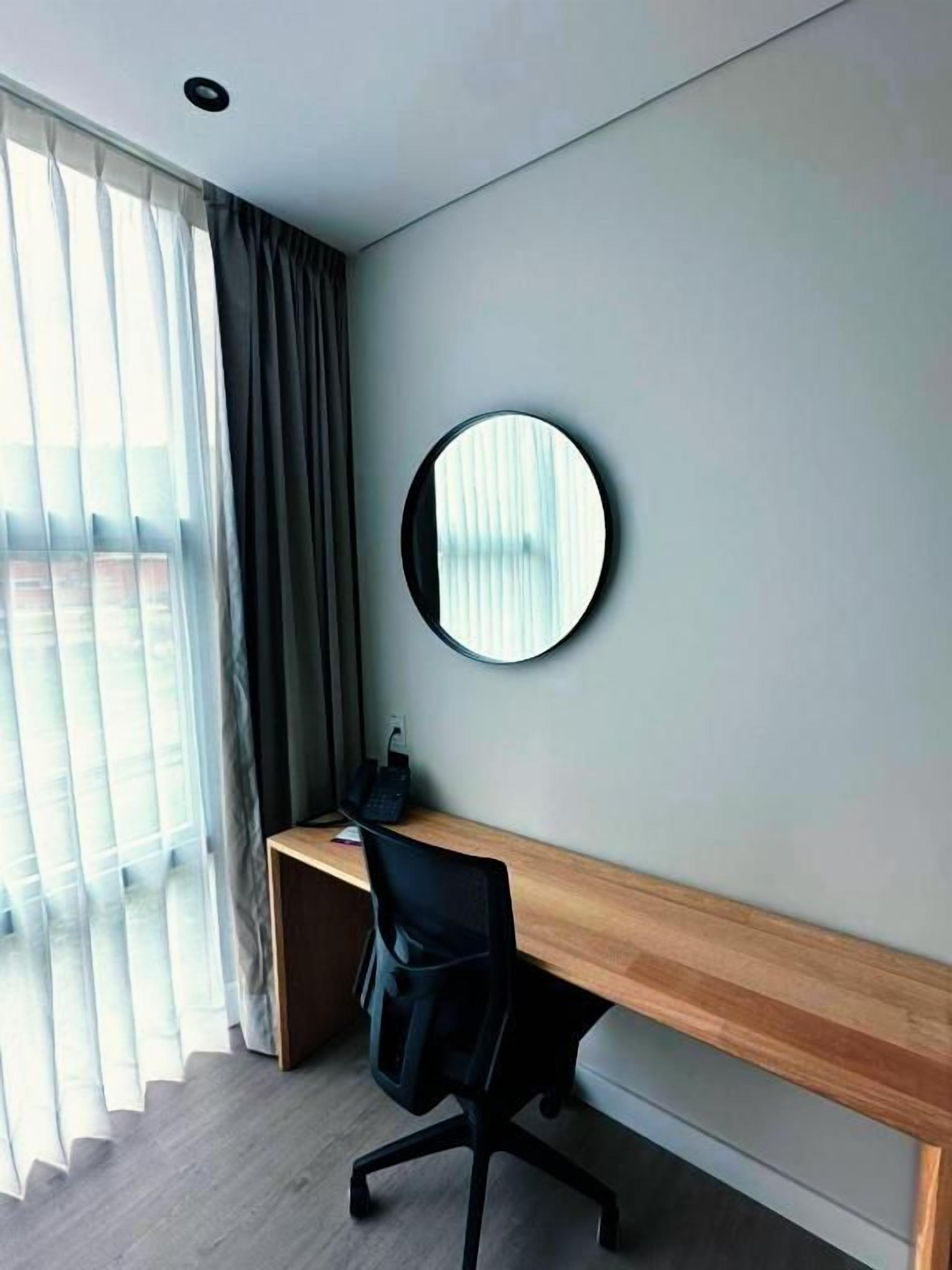 Una habitación de hotel con escritorio, silla y un espejo redondo en la pared.